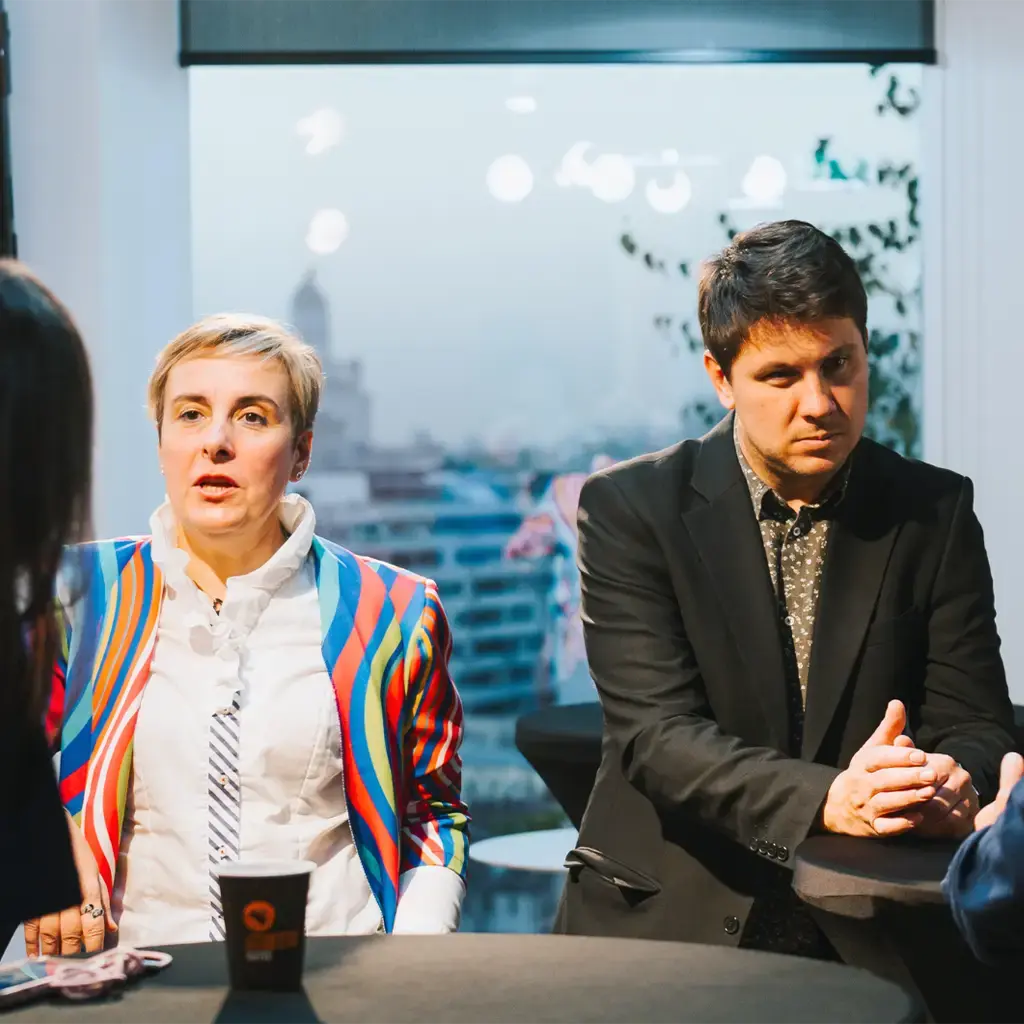 Group of professionals in discussion at a technology event with city view in background.