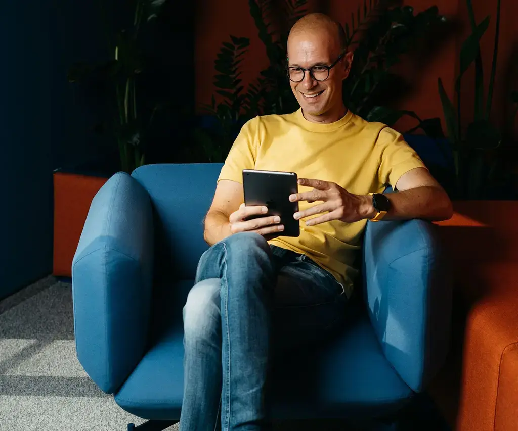 Person sitting on modern chair using a tablet in a relaxed, tech-focused office space.