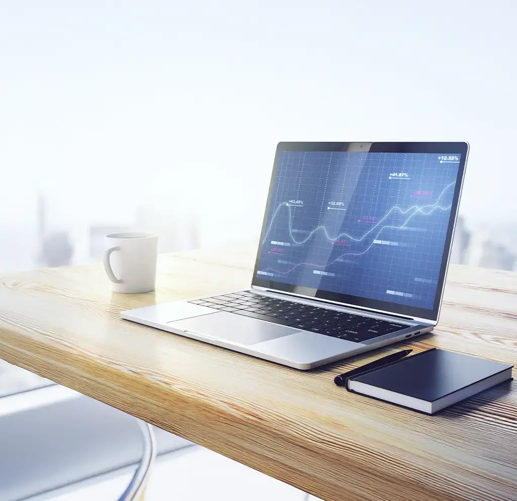Laptop displaying financial growth charts on a wooden desk with a notebook and coffee cup.