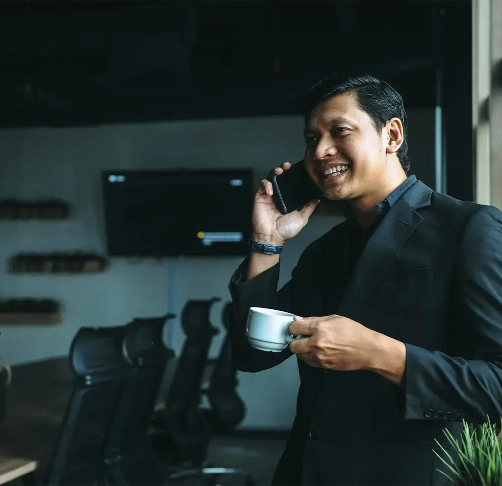 Professional in office holding coffee and talking on phone near window