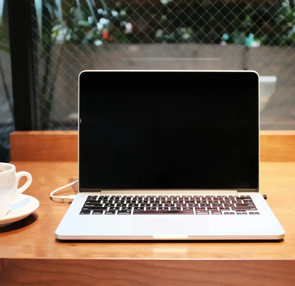 Open laptop and coffee cup on wooden desk by window in modern workspace