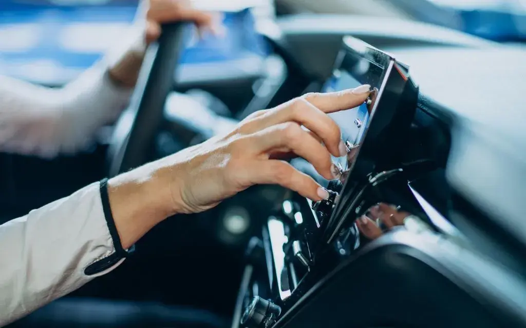 Person adjusting a touchscreen interface in a modern car dashboard.