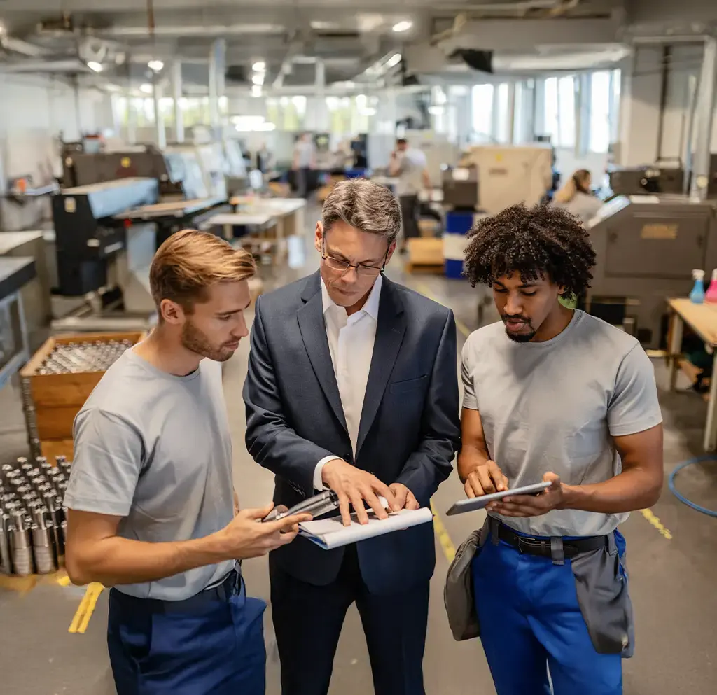 Factory manager and technicians reviewing production data on digital tablets in an industrial facility.