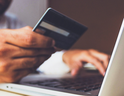 man hold his credit card while entering his information into the computer using payment processing