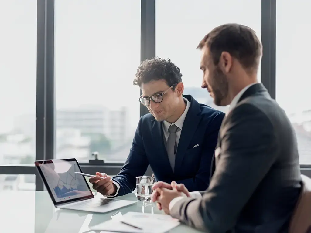 Two professionals review financial data on a laptop, discussing AI-driven insights in investment strategy.