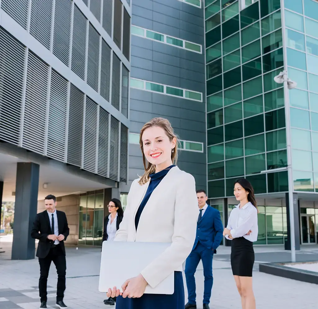 Business professionals standing outside a modern office building, one holding a closed laptop.