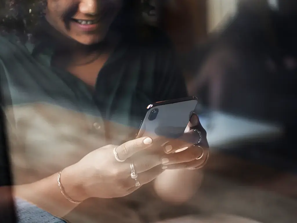 Person smiling while using a smartphone in a relaxed indoor setting.