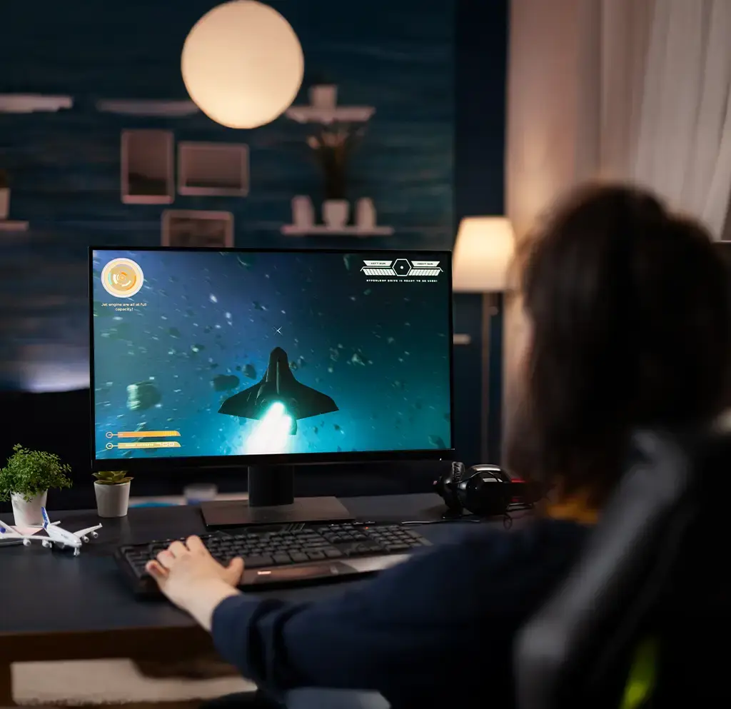 Person playing a space-themed video game on a desktop computer in a home setup.