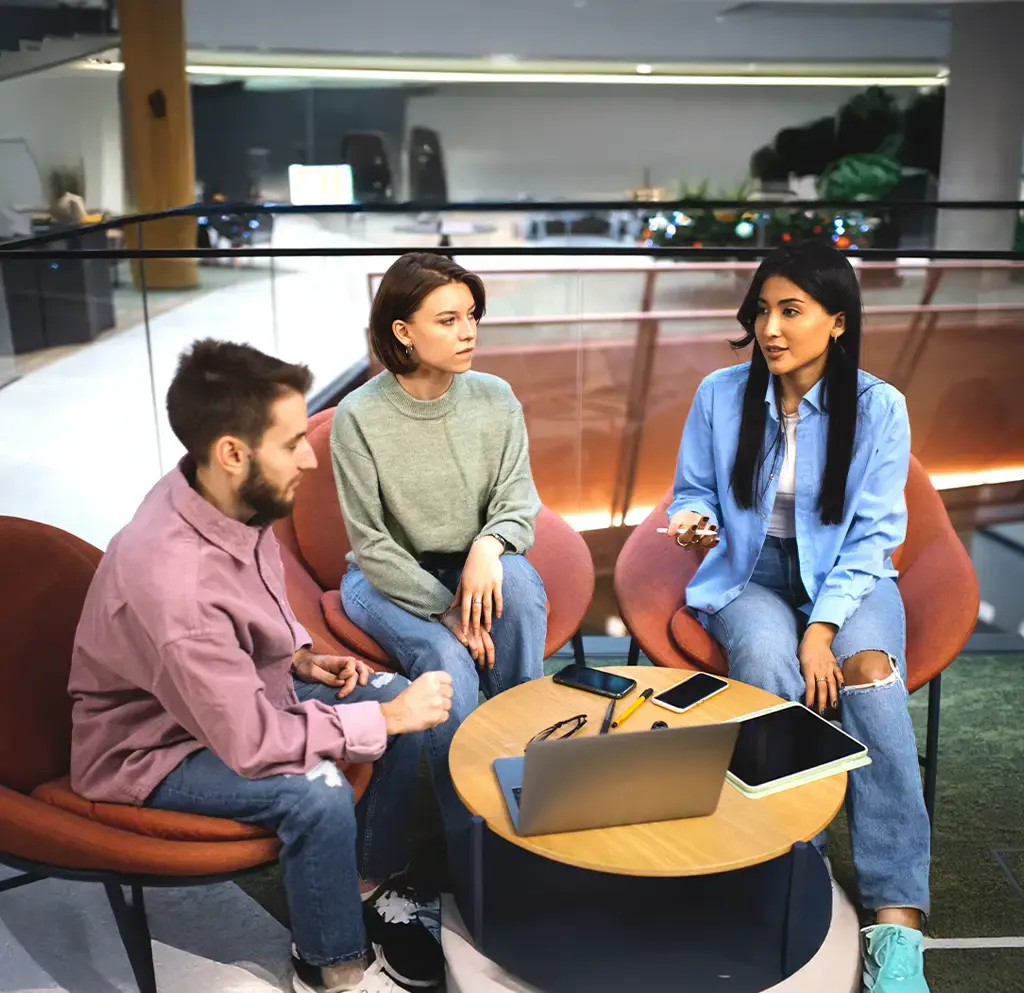 Team having a casual discussion around a laptop in a modern collaborative workspace.