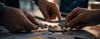 Hands connecting puzzle pieces on a map, representing collaborative problem-solving and strategic delivery