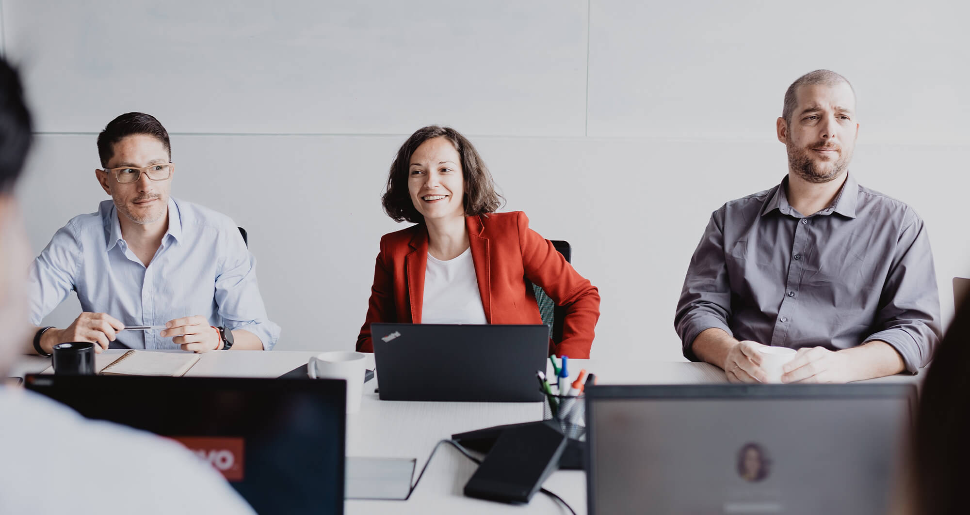 Professionals engaged in a collaborative meeting around a conference table with laptops open.