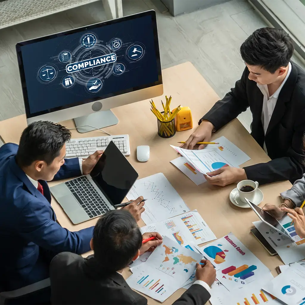 Team collaborating on compliance strategy with charts and digital reports in modern office.