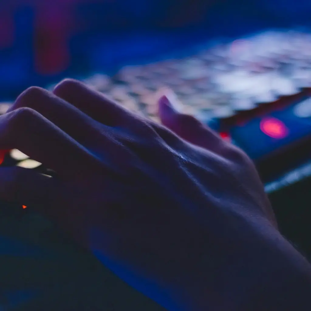 Hands typing on illuminated keyboard in a dark workspace, representing software development and digital engineering