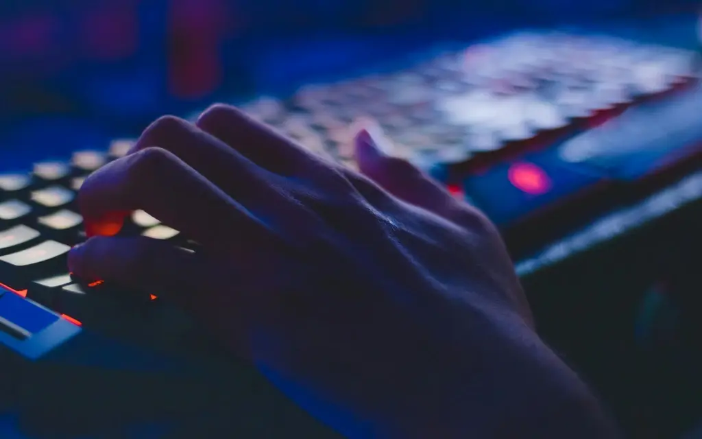 Hands typing on illuminated keyboard in a dark workspace, representing software development and digital engineering
