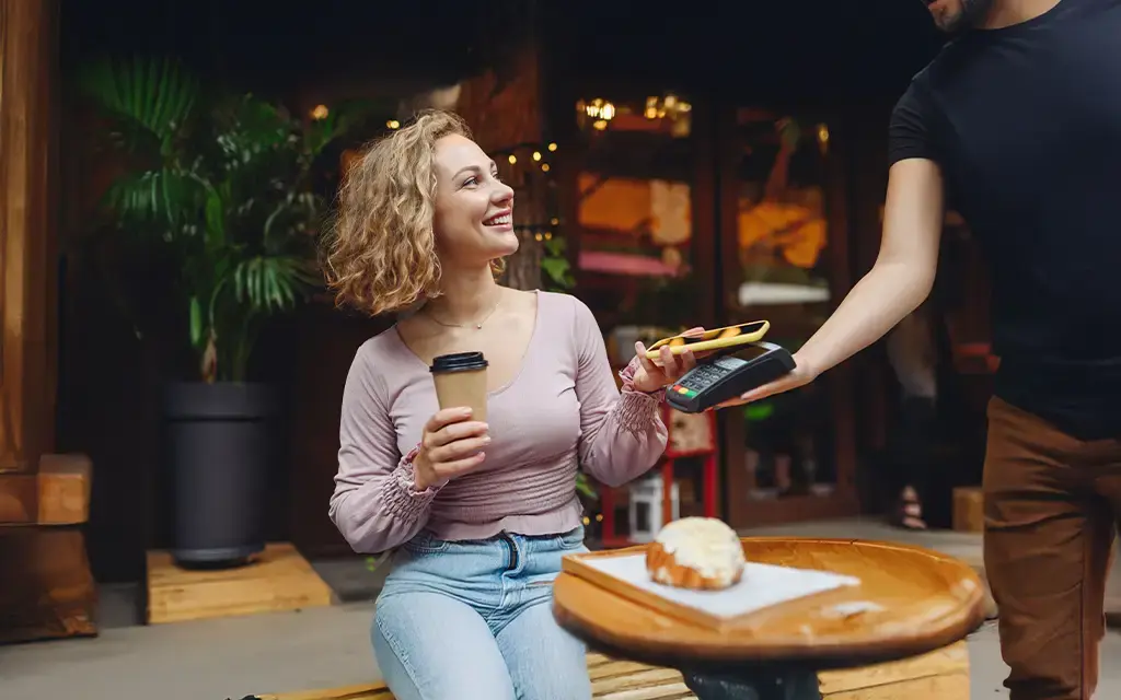 Customer uses contactless mobile payment at a cafe while holding coffee