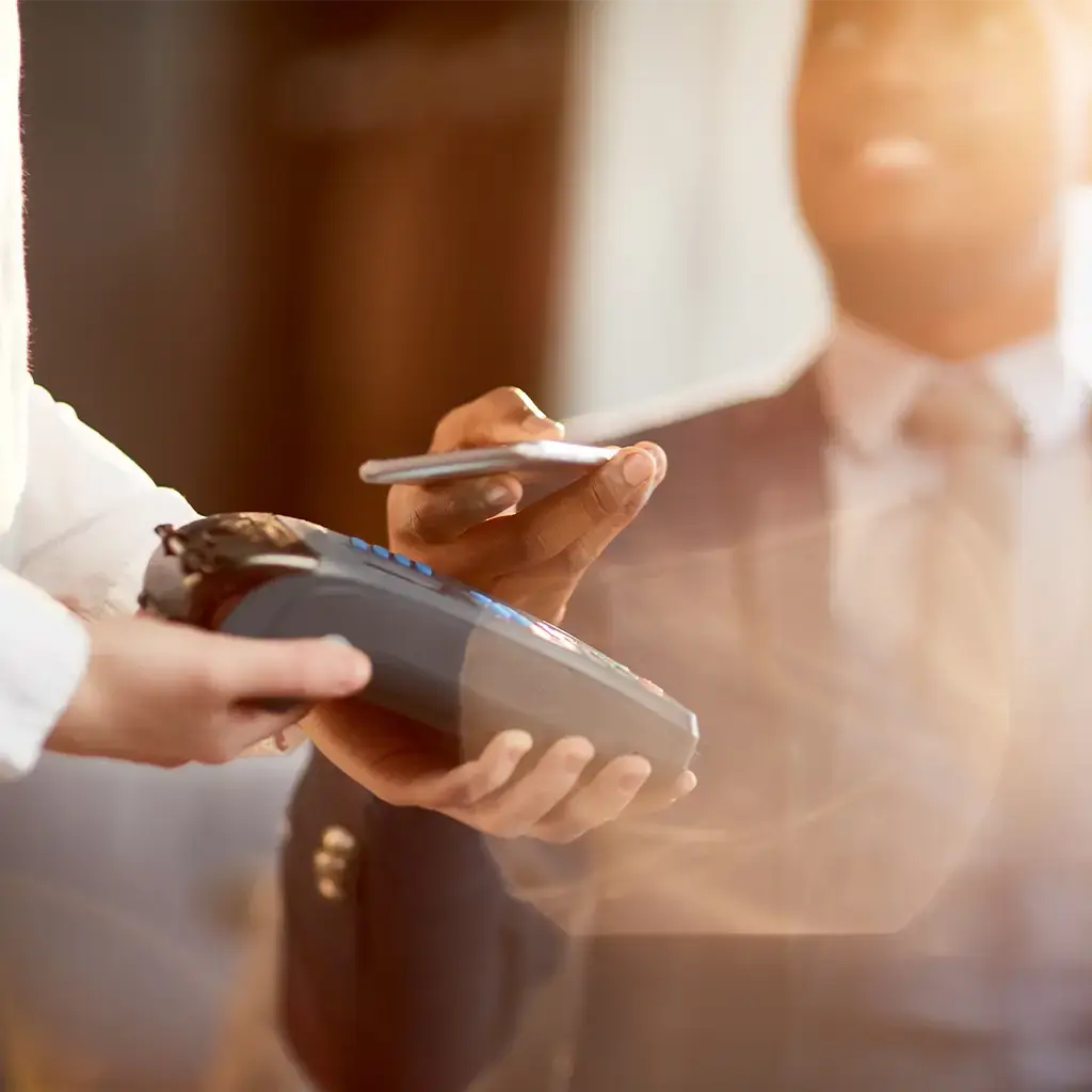 Customer using smartphone for contactless payment on a card reader in a business setting.