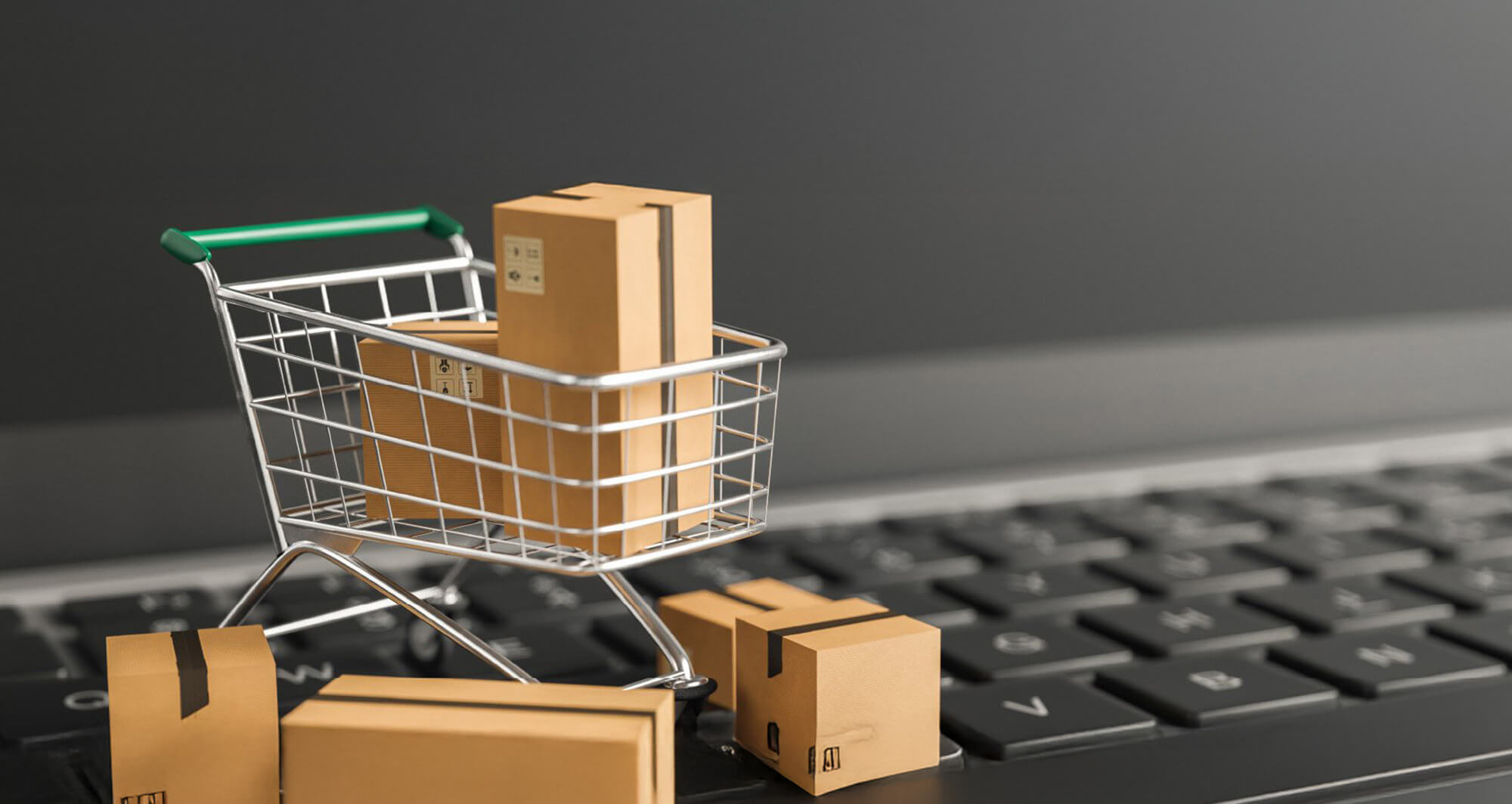 Mini shopping cart with parcels on a laptop keyboard, symbolizing digital commerce and online fulfillment.
