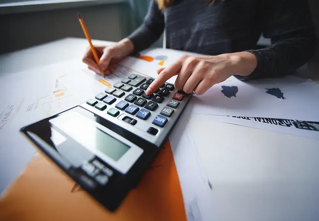 Person using a calculator while reviewing retail dynamic pricing data on printed reports.