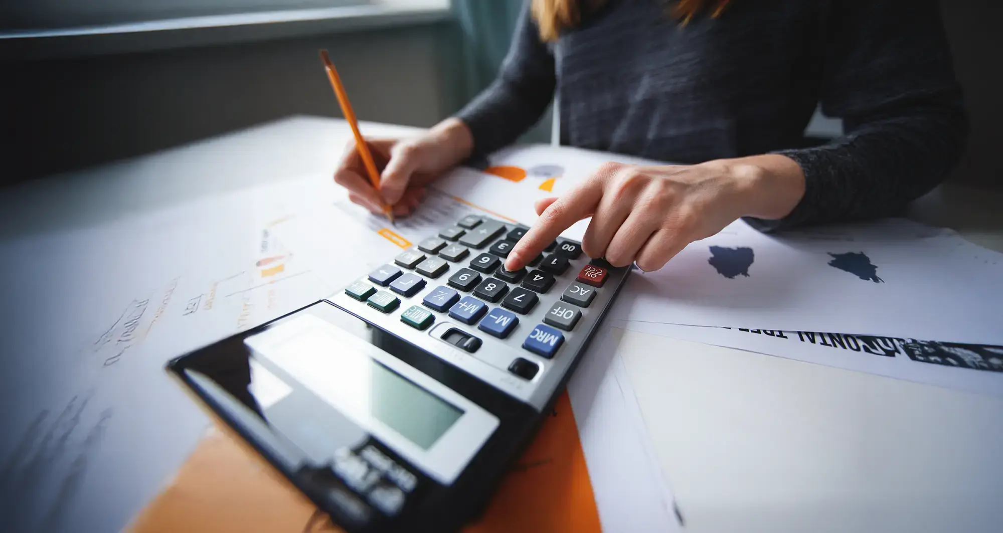 Person using a calculator while reviewing retail dynamic pricing data on printed reports.