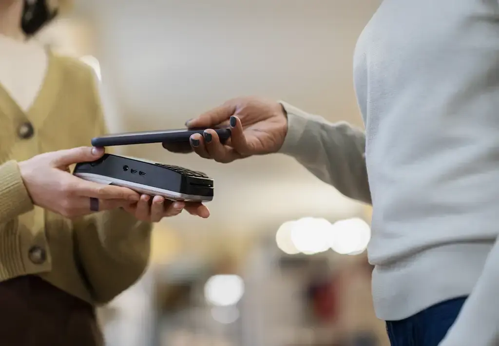 Customer making a contactless payment using a smartphone and card reader in a retail environment.