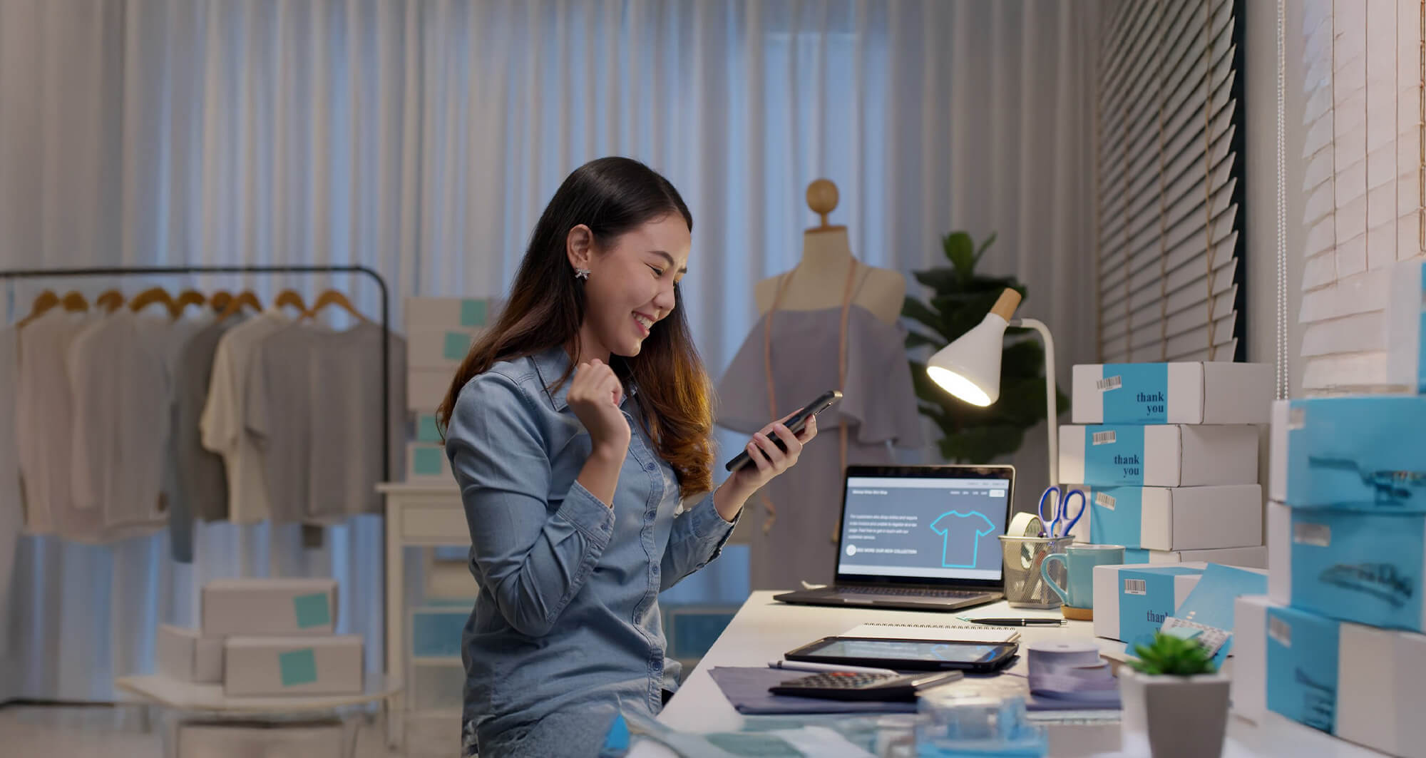 Small business owner celebrating an online sale in a home-based retail workspace with packed orders.