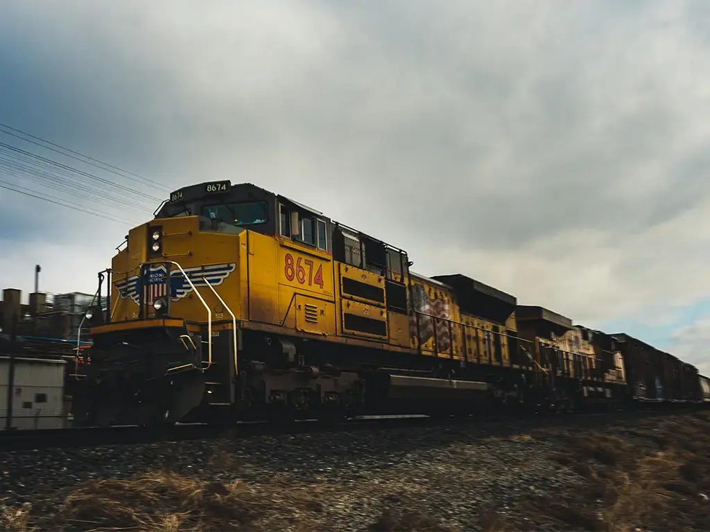 Yellow freight train traveling on a railway track under a cloudy sky, representing logistics and transportation services.