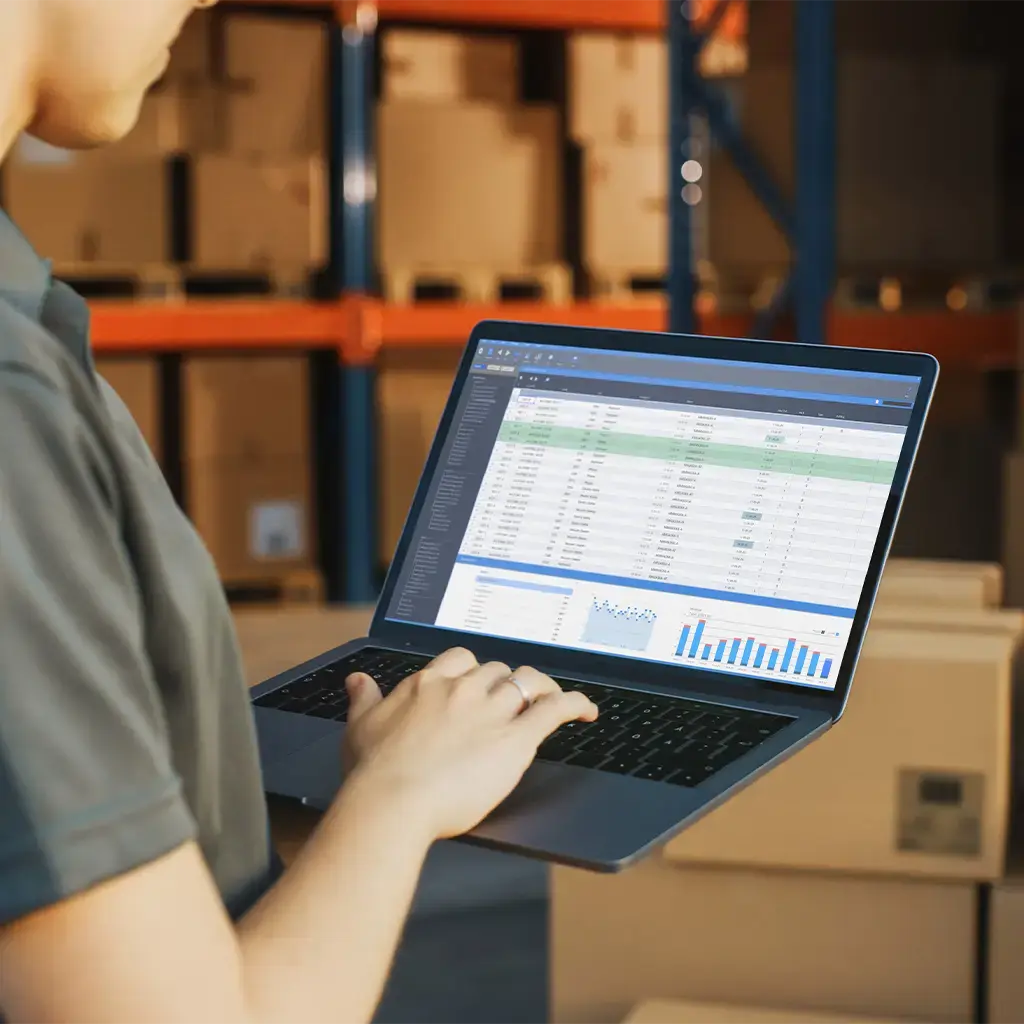Employee using logistics software on a laptop to manage warehouse inventory and shipping data.