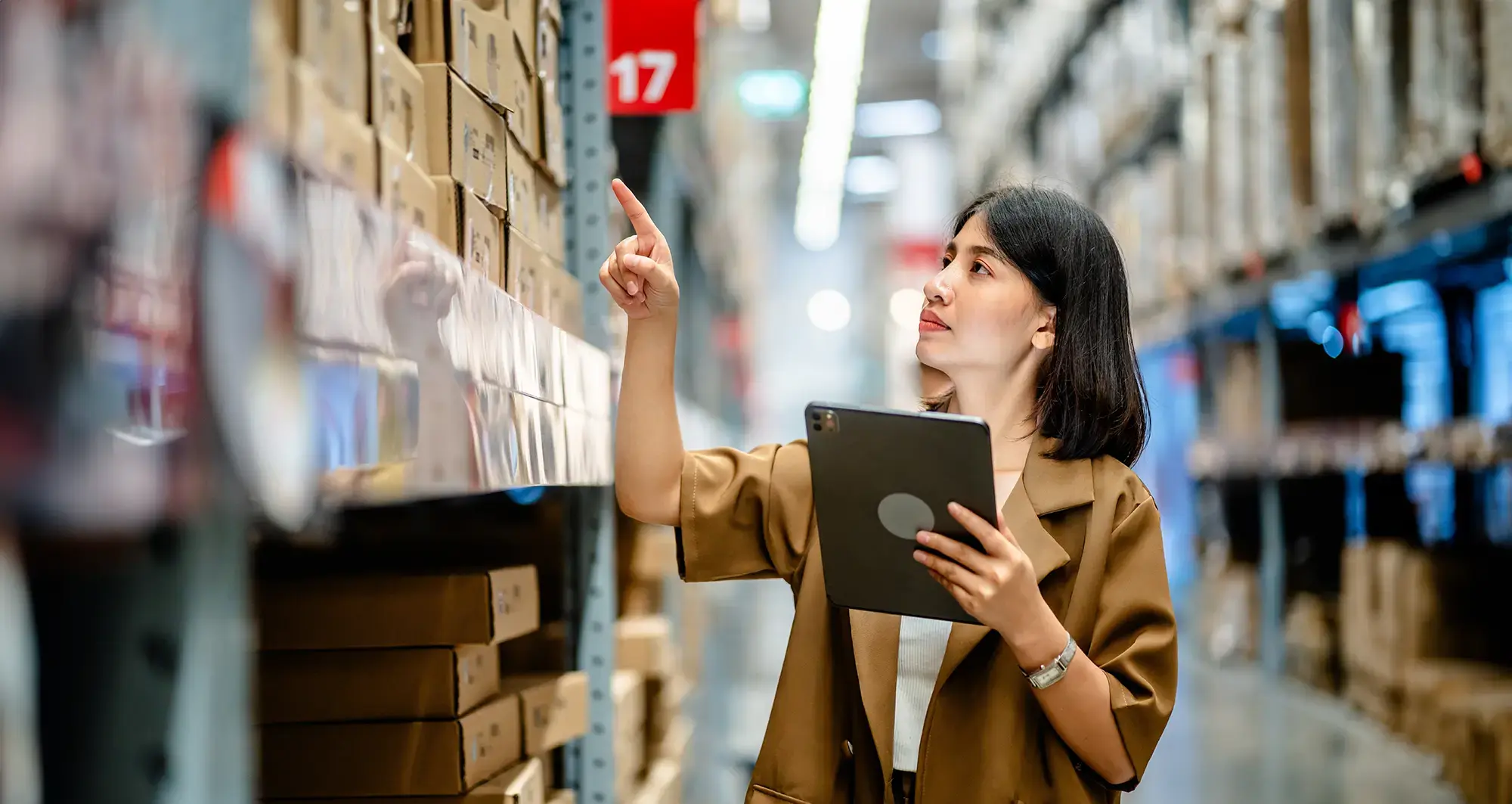 woman pointing to item on warehouse shelf while holding a tablet