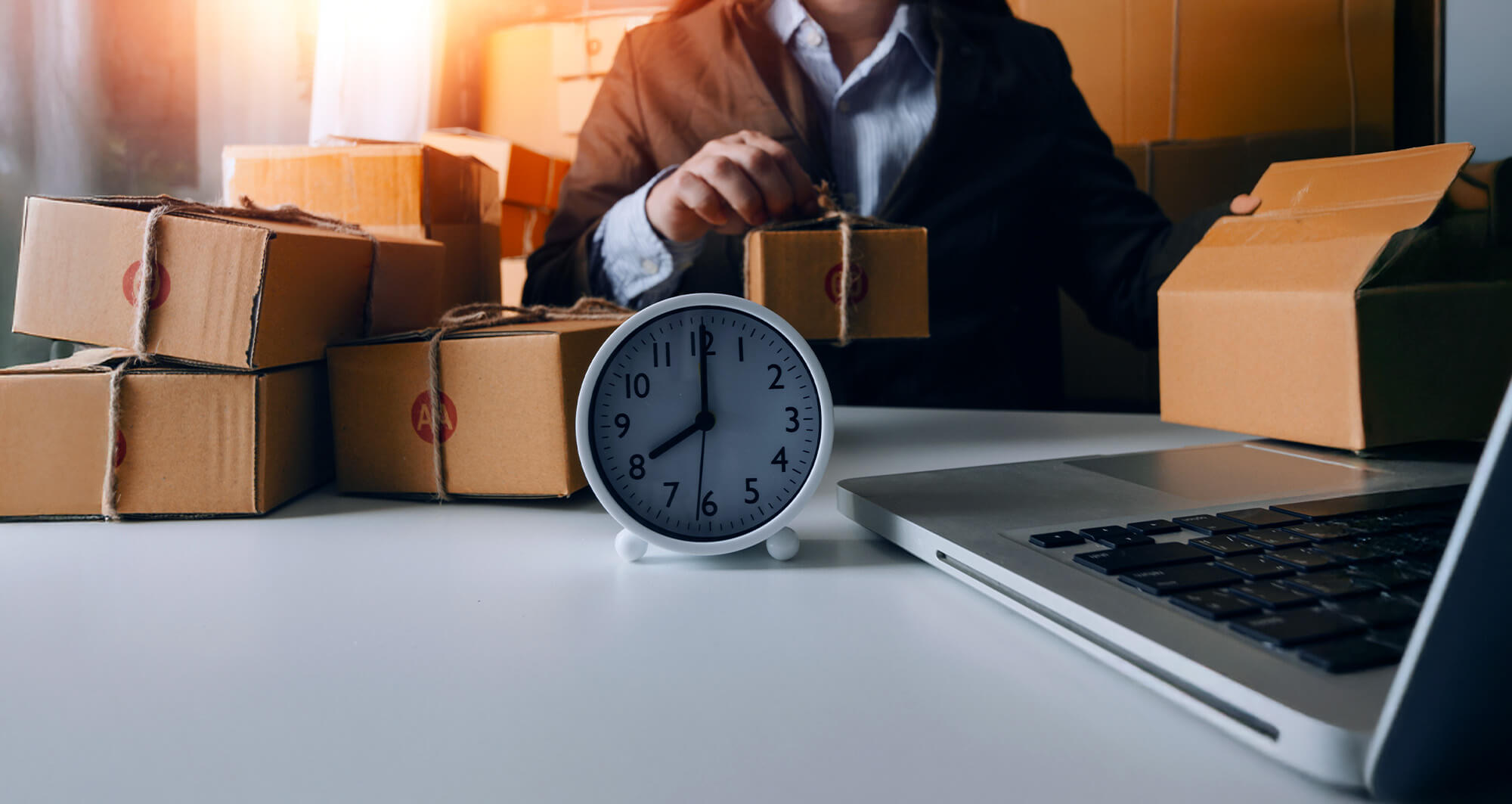 Person handling delivery boxes near laptop and clock, representing efficient supply chain operations.