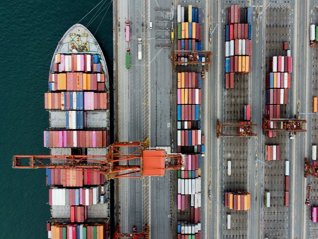 Aerial view of a cargo ship and shipping containers at a port, illustrating global supply chain and logistics operations.