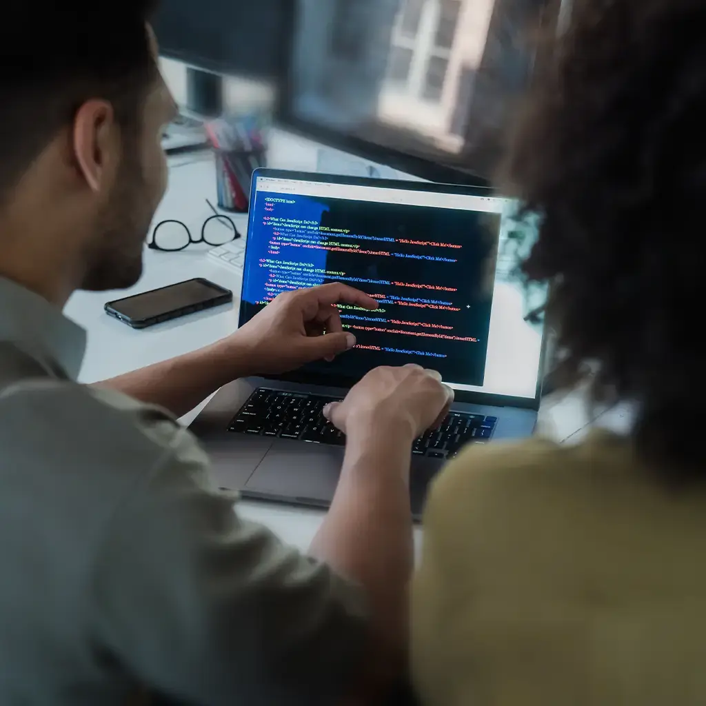 Software engineers reviewing code on a laptop to accelerate AI-powered software delivery and development.
