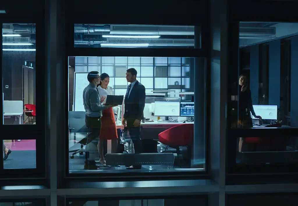 Teams collaborating in a modern office at night, focused on digital project development.