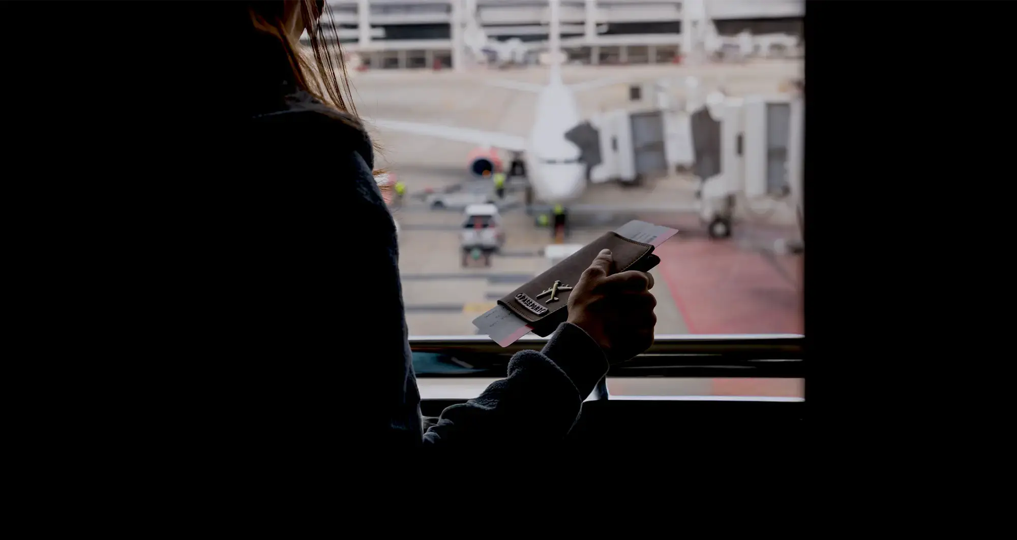 Woman holding a passport while looking at a airport's window