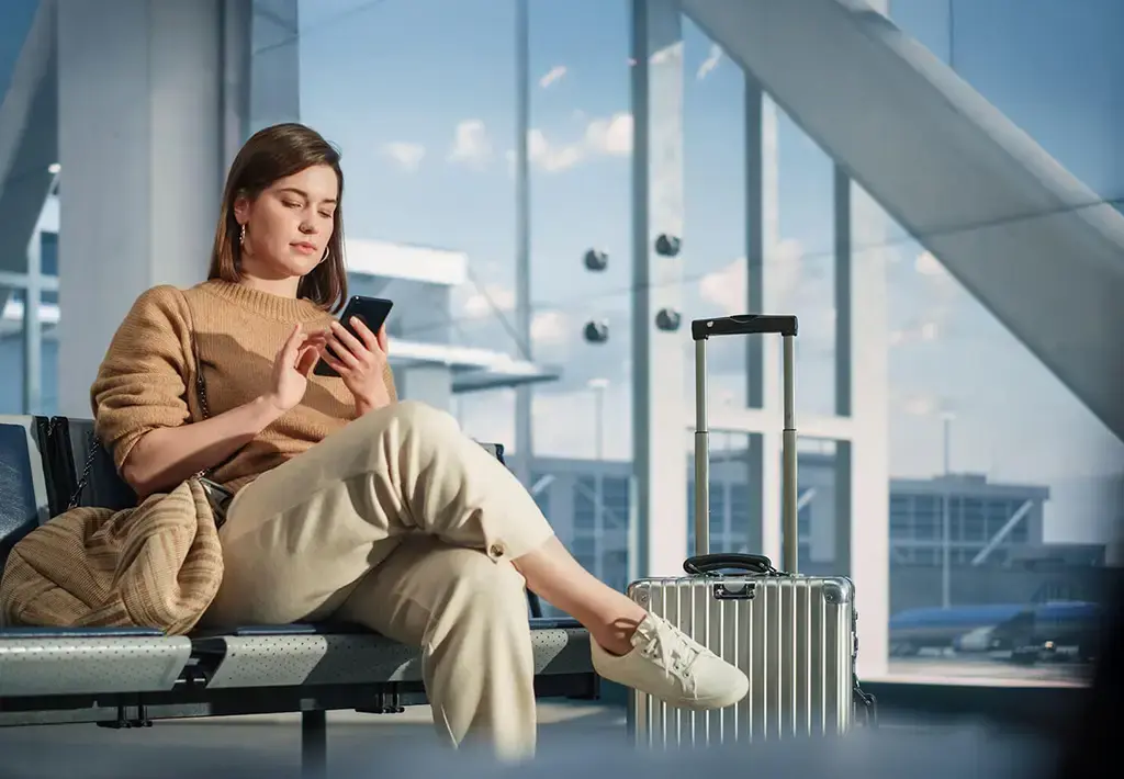 Traveler using mobile device at airport, reflecting digital transformation in aviation services.