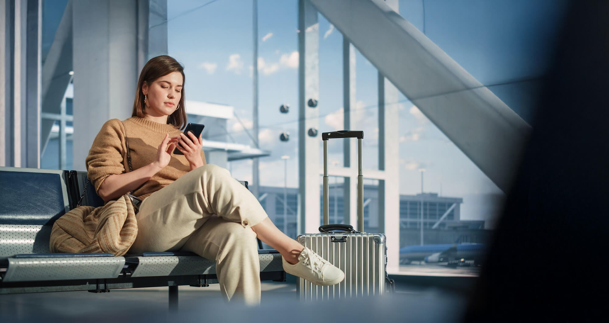 Traveler using mobile device at airport, reflecting digital transformation in aviation services.