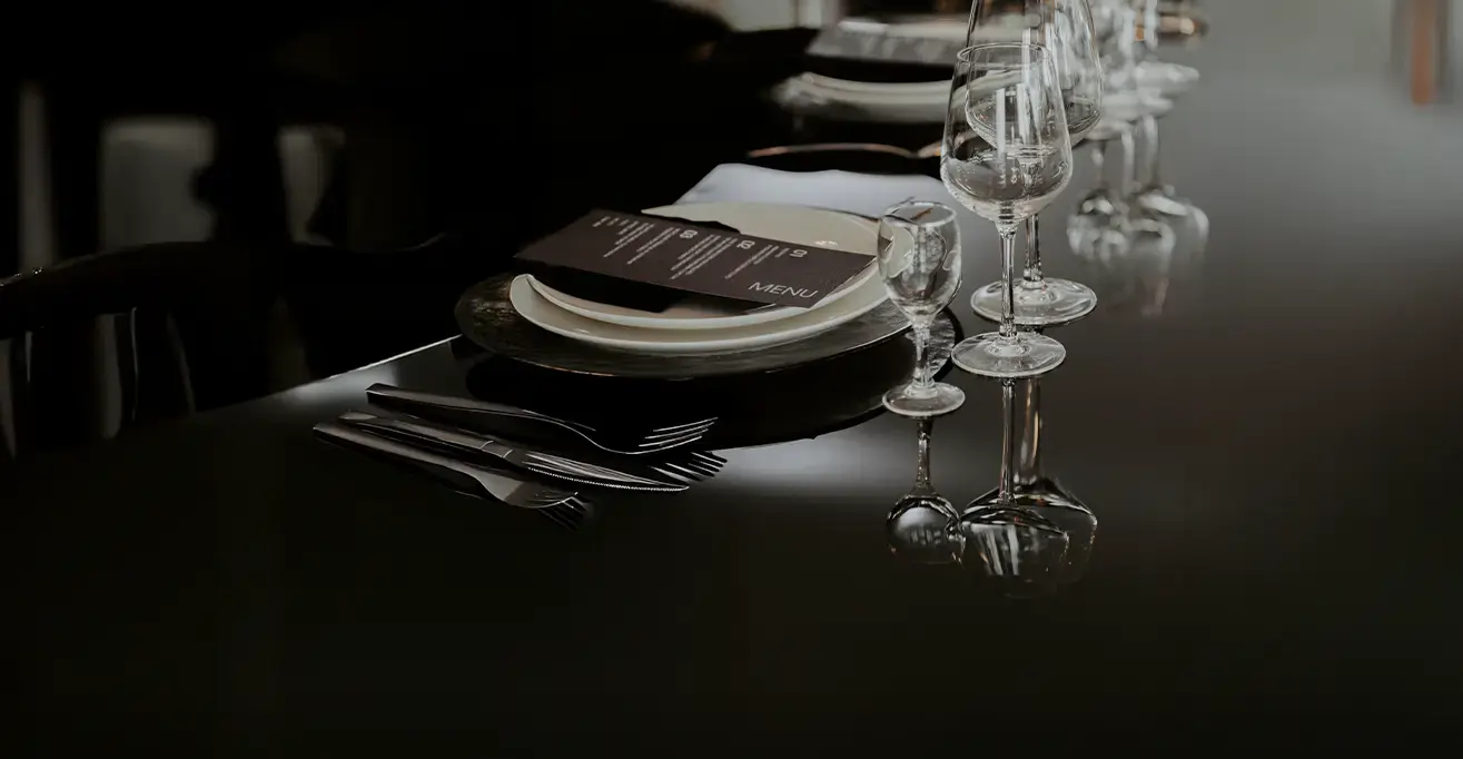 Elegant table setting with plates, glassware, cutlery, and a printed menu on a glossy black surface.