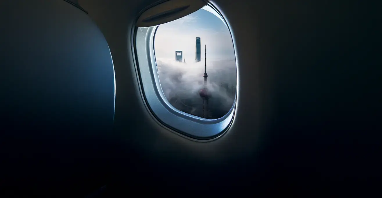City skyscrapers emerging through clouds, viewed from an airplane window during flight.