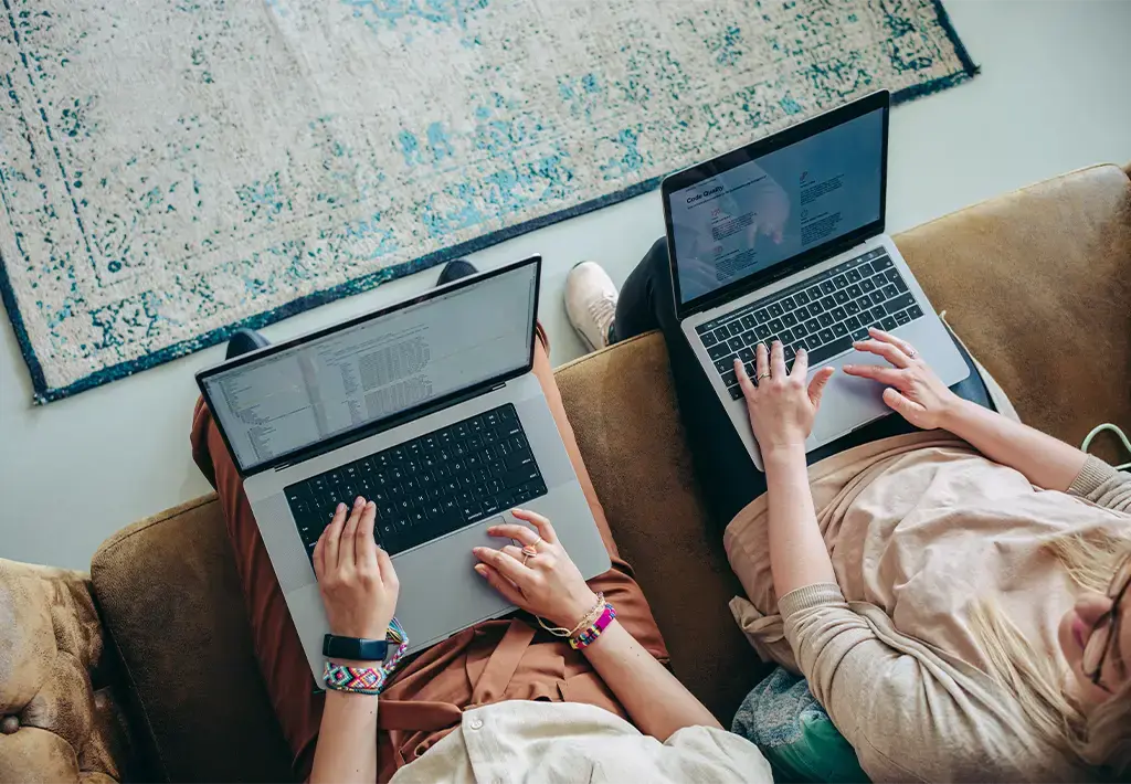 Two people collaborating on laptops, working on code and documents in a casual setting.