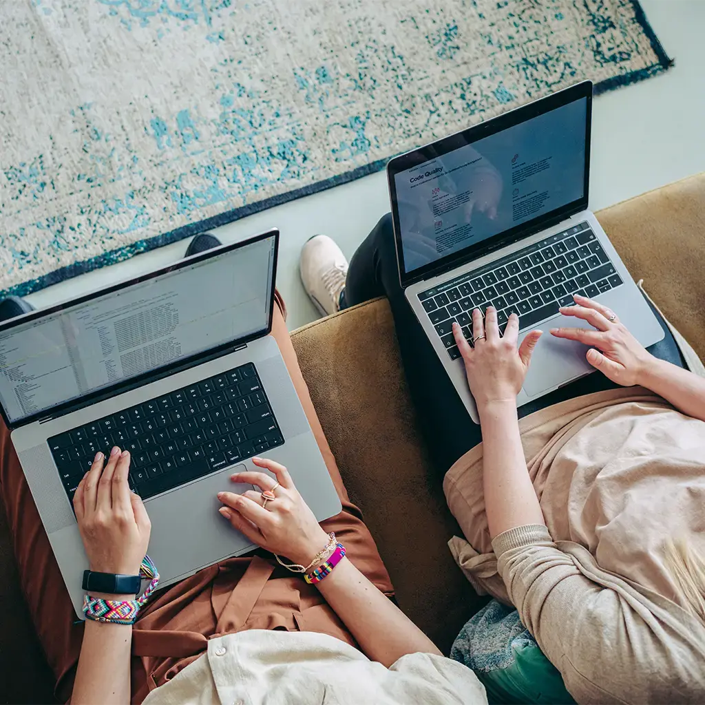 Two people collaborating on laptops, working on code and documents in a casual setting.