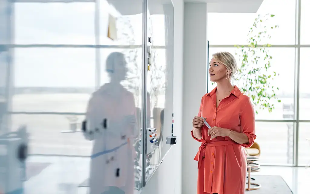 Professional reviewing notes on a whiteboard in a modern, bright office environment.