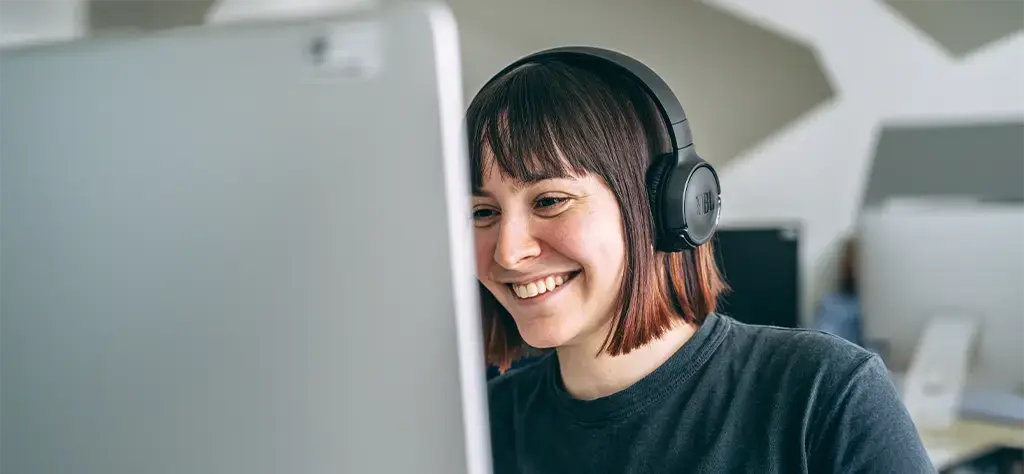 early career employee working at computer station with earphones