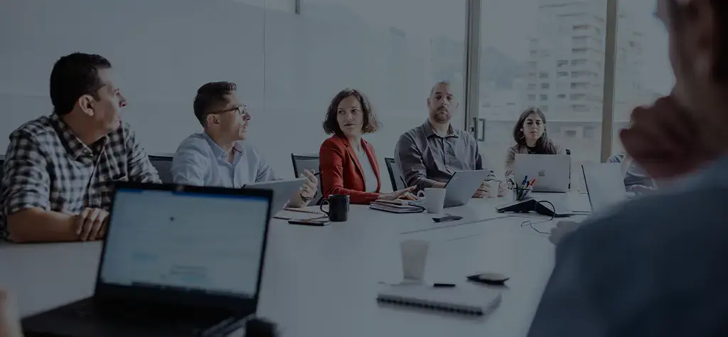Team members in a strategy meeting around a conference table with laptops and notepads.
