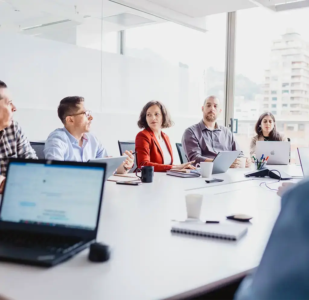 Team members in a strategy meeting around a conference table with laptops and notepads.