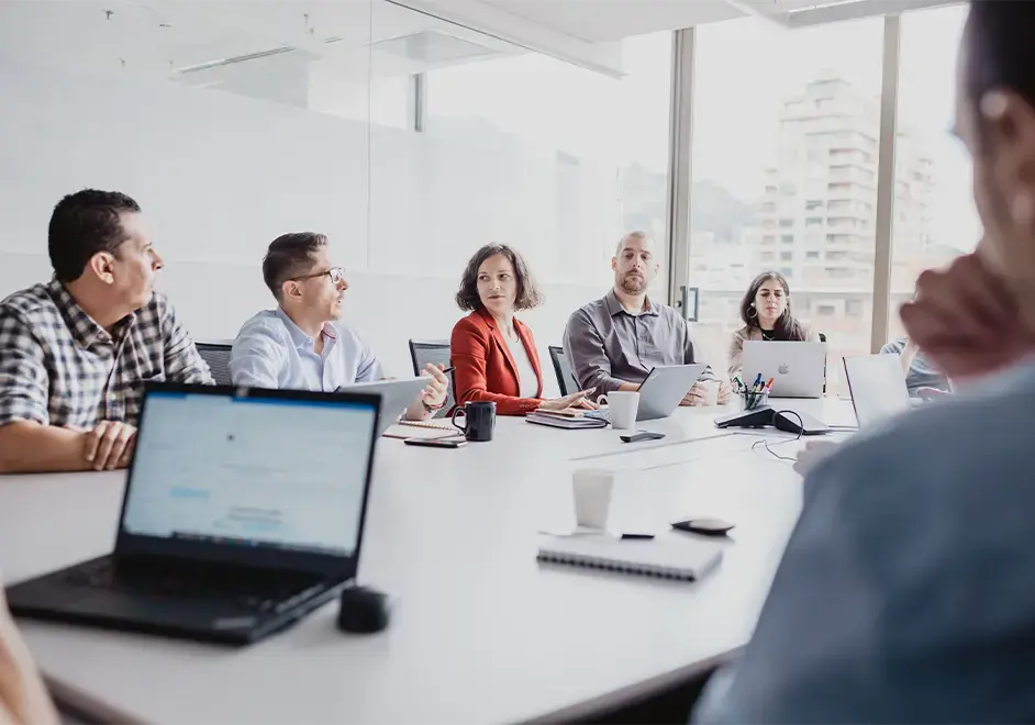 Team members in a strategy meeting around a conference table with laptops and notepads.
