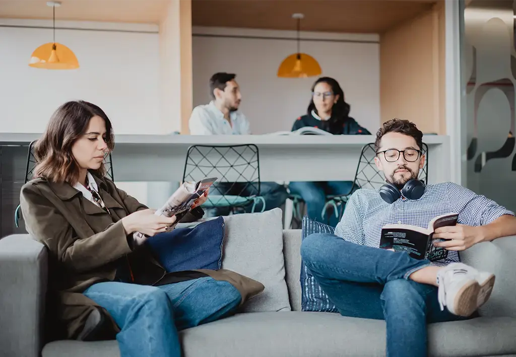 Team members relaxing and reading in a modern, collaborative office lounge.