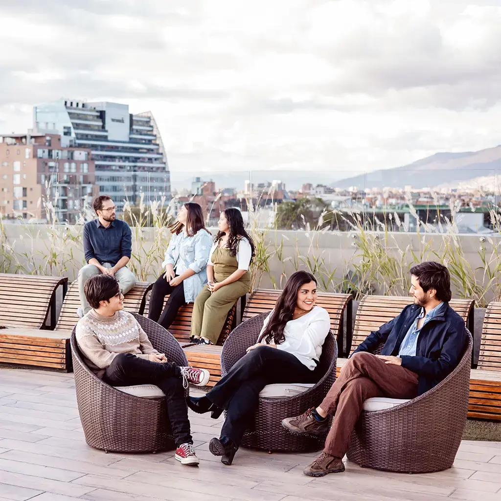 Colleagues chatting and relaxing on a rooftop terrace with a city skyline, suggesting workplace collaboration.