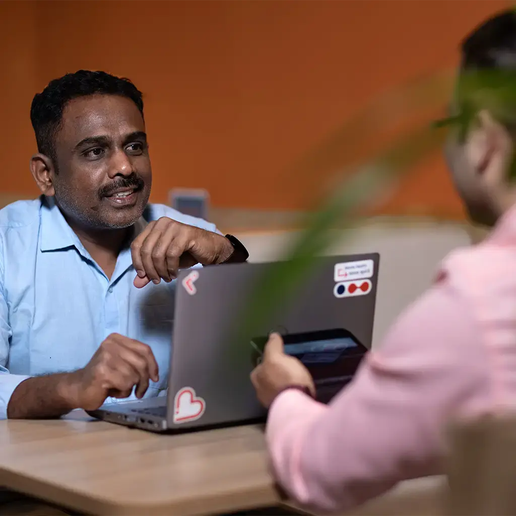 Two professionals in discussion at a table with laptops in a modern office setting.