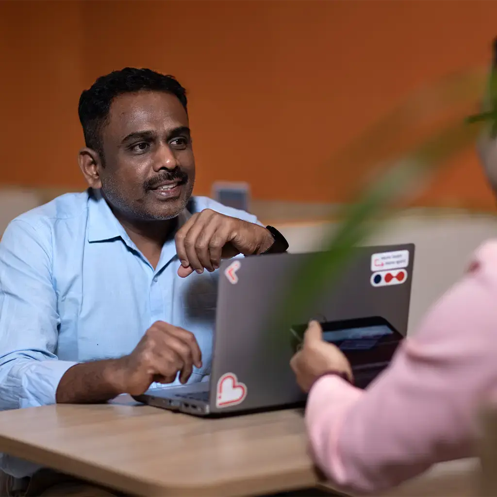 Two professionals in discussion at a table with laptops in a modern office setting.