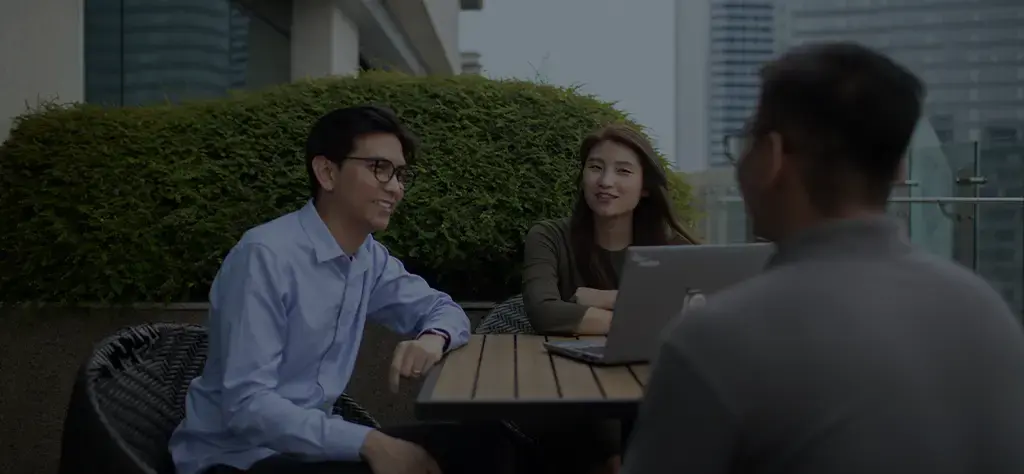 Colleagues having a business discussion on a rooftop terrace with a laptop open on the table.