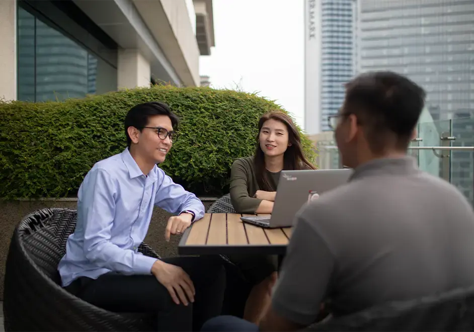 Colleagues having a business discussion on a rooftop terrace with a laptop open on the table.